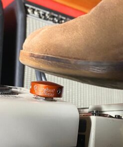 A shoe pressing a Barefoot Buttons V1 Standard Orange footswitch topper installed on a guitar pedal.
