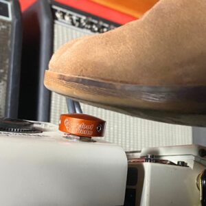 A shoe pressing a Barefoot Buttons V1 Standard Orange footswitch topper installed on a guitar pedal.