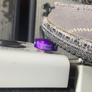 Close-up of a Barefoot Buttons V1 Standard Purple footswitch topper installed on a guitar pedal, pressed with a shoe.