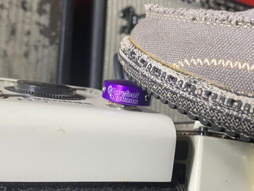 Close-up of a Barefoot Buttons V1 Standard Purple footswitch topper installed on a guitar pedal, pressed with a shoe.