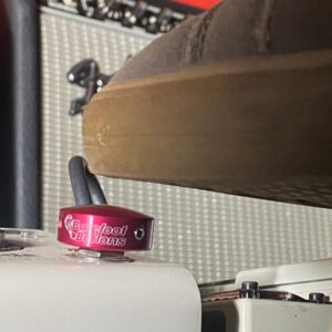A shoe pressing a Barefoot Buttons V1 Standard Red footswitch topper installed on a guitar pedal.