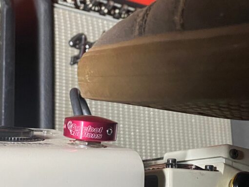 A shoe pressing a Barefoot Buttons V1 Standard Red footswitch topper installed on a guitar pedal.