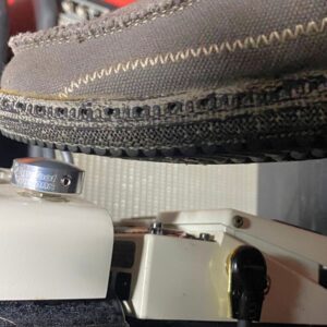 A shoe pressing a Barefoot Buttons V1 Standard Silver footswitch topper installed on a white guitar pedal.