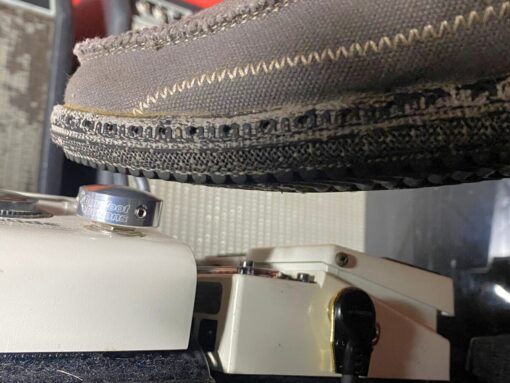 A shoe pressing a Barefoot Buttons V1 Standard Silver footswitch topper installed on a white guitar pedal.
