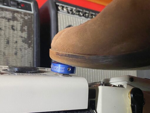 A shoe pressing a Barefoot Buttons V1 Standard Dark Blue footswitch topper installed on a guitar pedal.