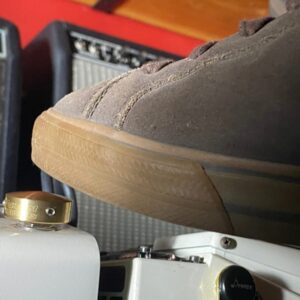 Close-up of a Barefoot Buttons V1 Standard Brass footswitch topper installed on a guitar pedal, pressed with a shoe.