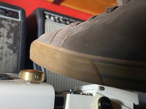 Close-up of a Barefoot Buttons V1 Standard Brass footswitch topper installed on a guitar pedal, pressed with a shoe.